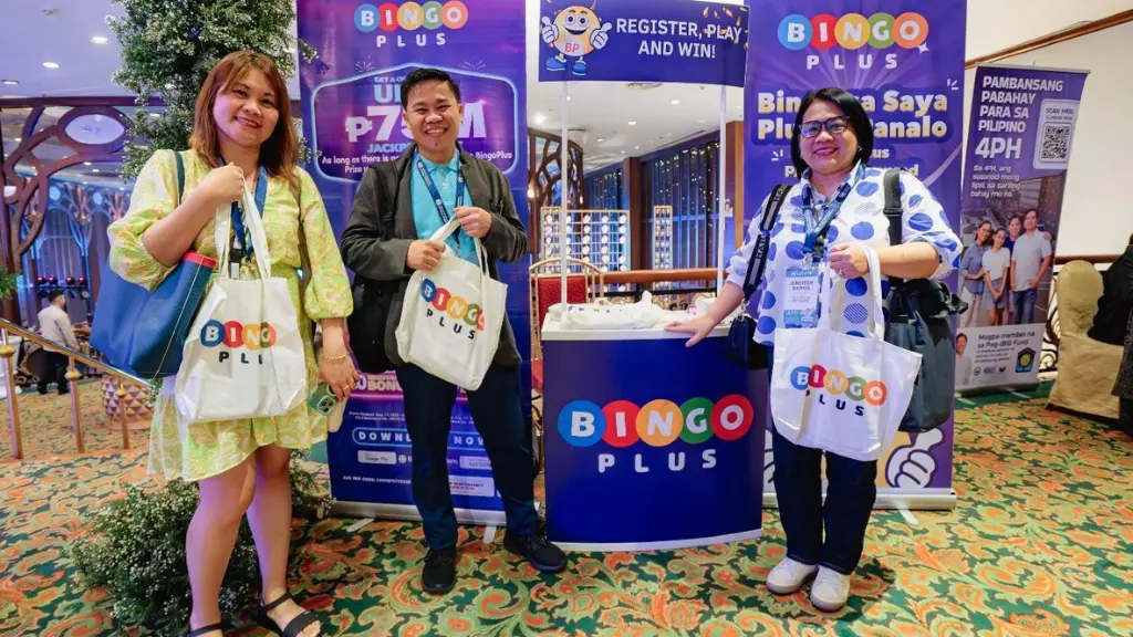 Media persons posing in front of the BingoPlus booth holding some give-away merchandise.